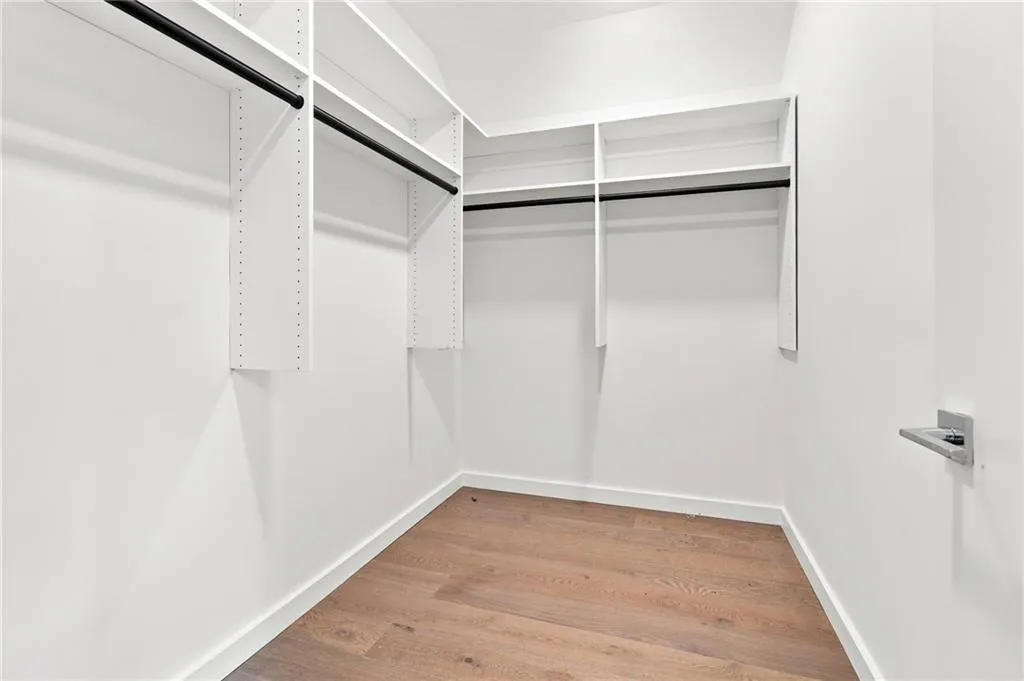 Walk-in closet with wood-finish flooring, white walls, built-in shelving, and black hanging rods