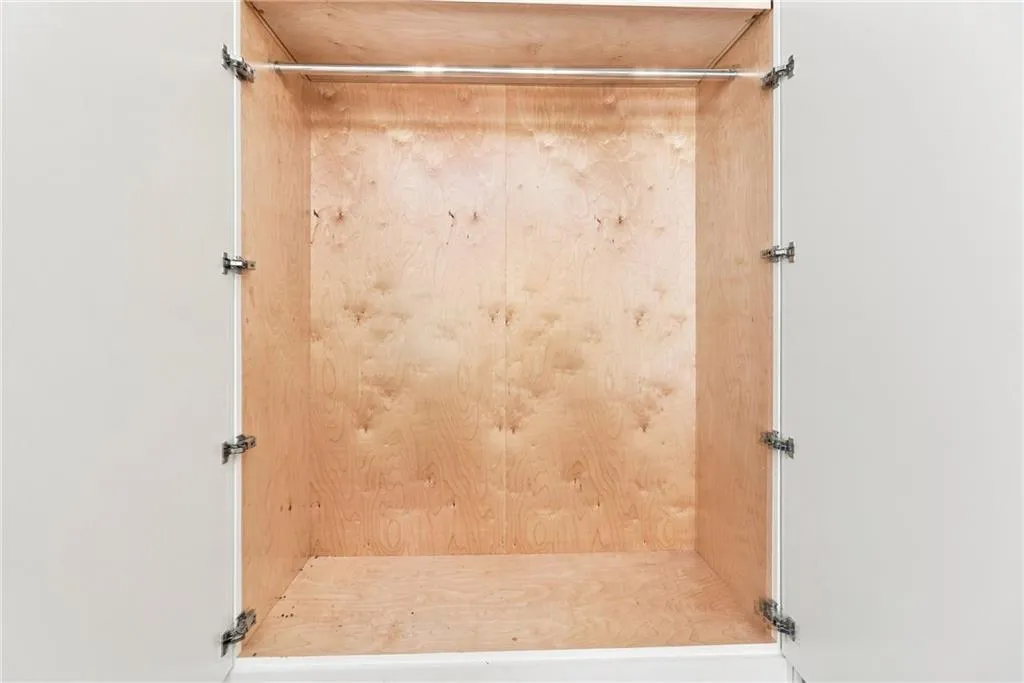 Built-in closet with natural wood-finish interior, white cabinetry, and a chrome hanging rod