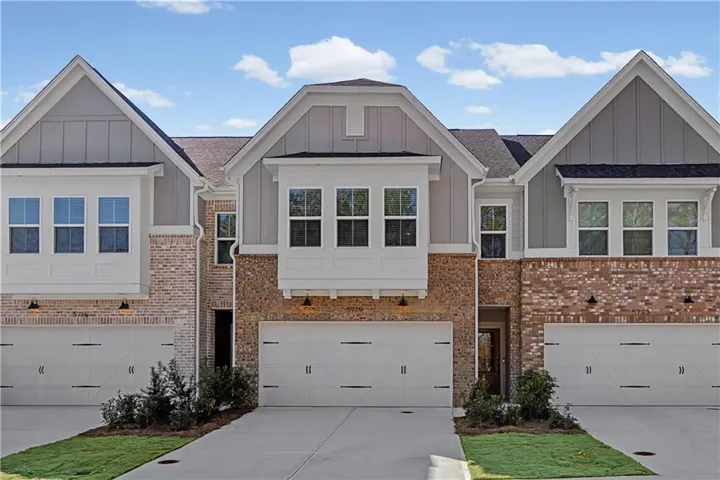 Contemporary brick and siding townhome featuring a two-car garage, dormer windows, and a covered entryway