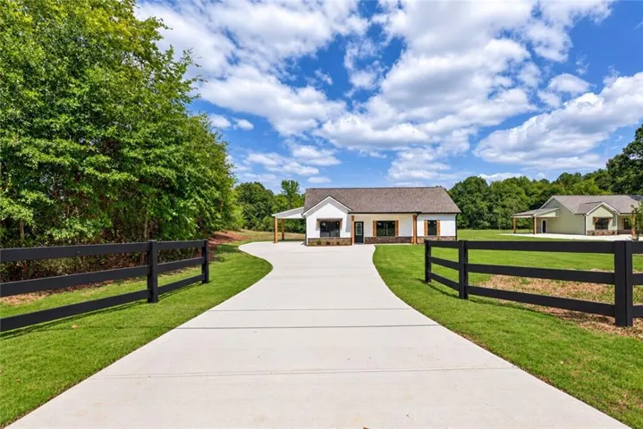 Paved driveway leading to a white exterior home with a covered entryway, dark trim windows, and a dark shingle roof