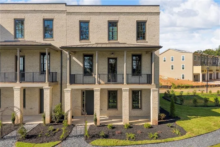 Brick facade, multiple covered balconies, ground-level covered porch, dark-framed windows, and manicured landscaping