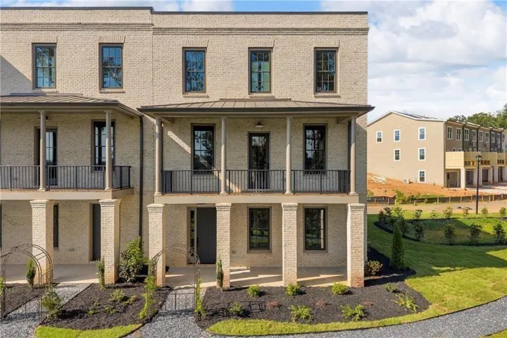 Brick facade, multiple covered balconies, ground-level covered porch, dark-framed windows, and manicured landscaping