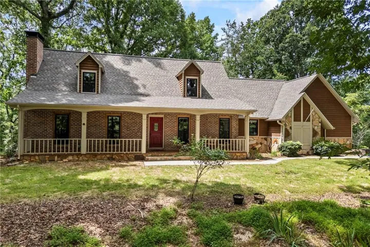 Traditional-style residence featuring a brick facade, covered front porch with white railing, dormer windows, a prominent brick chimney, and natural stone accents