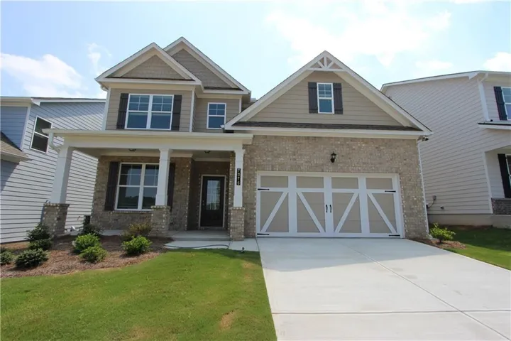 Two-story residence featuring a brick facade, covered front porch, and a two-car garage with decorative hardware