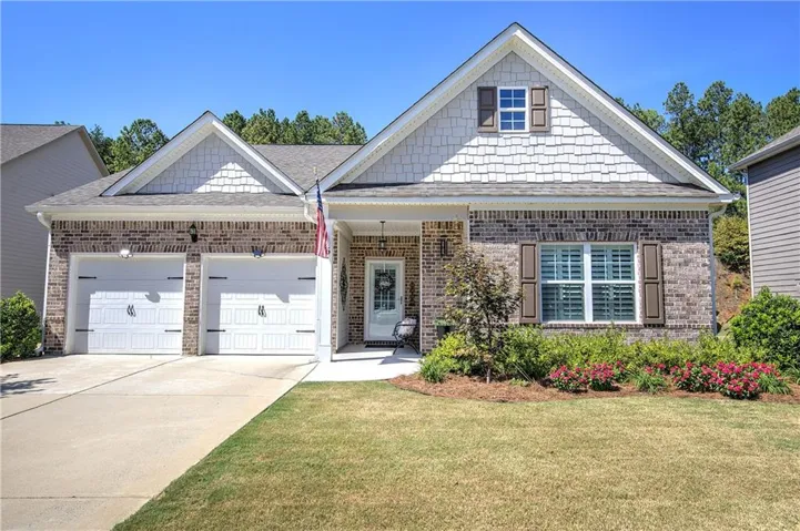 Brick and shingle exterior with a covered entry, two-car garage, manicured lawn, and mature landscaping