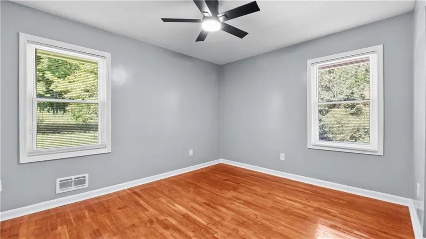 Room featuring wood-finish flooring, light grey walls, white trim, and two windows
