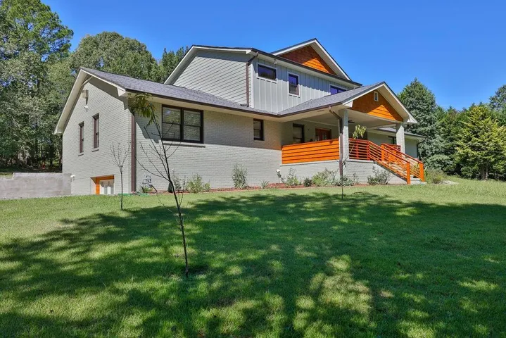View of front facade featuring board and batten siding, covered porch, a front lawn, and brick siding