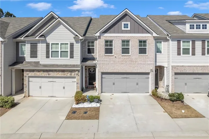 Multi-story townhouse featuring a brick and siding exterior, two-car garage, and integrated landscaping