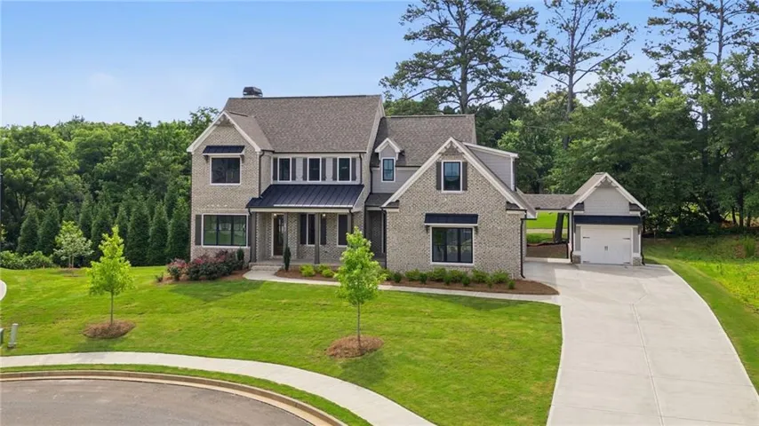 Two-story residence featuring light gray brick and siding, a covered entryway, and a prominent metal roof accent