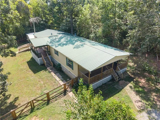 Expansive property featuring a green metal roof, covered front porch, wood-slat fencing, and mature trees