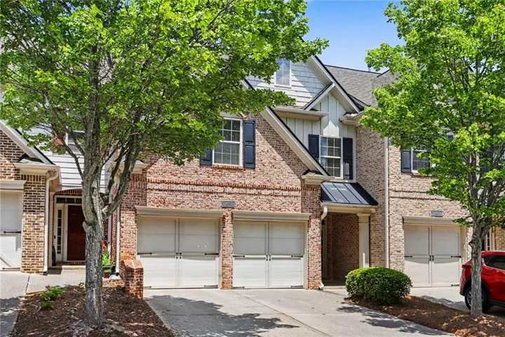 Brick facade townhome featuring two garage bays with roll-up doors, a covered entry, and dark window shutters