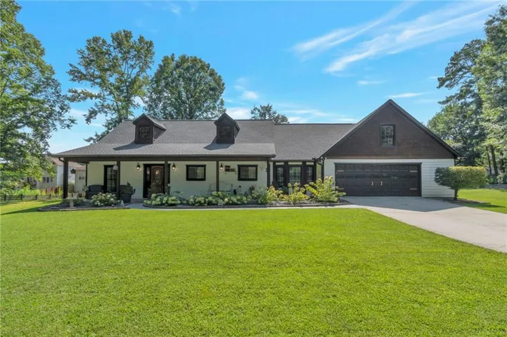 Expansive front lawn, covered porch, dormer windows, attached garage, and paved driveway