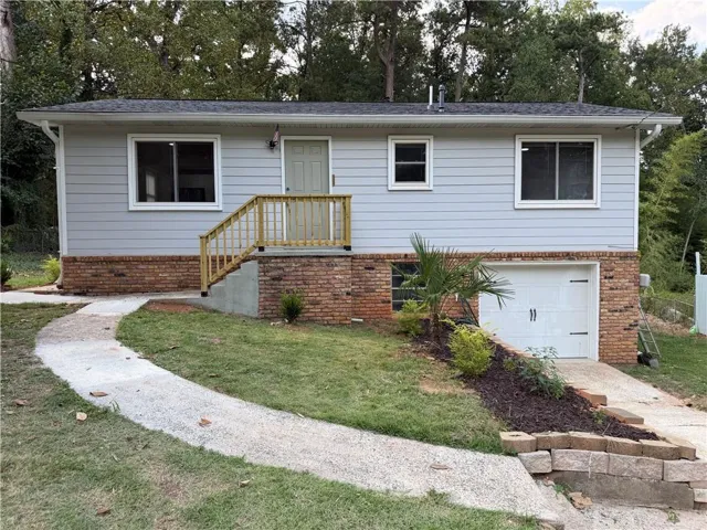 Siding exterior with brick foundation, front entry with wood railing, attached garage, and a concrete pathway