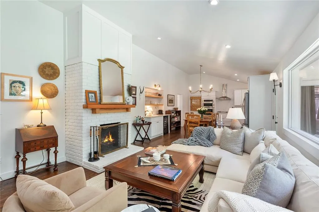 Living area with vaulted ceiling, a brick fireplace, dark wood-style flooring, a chandelier, and recessed lighting