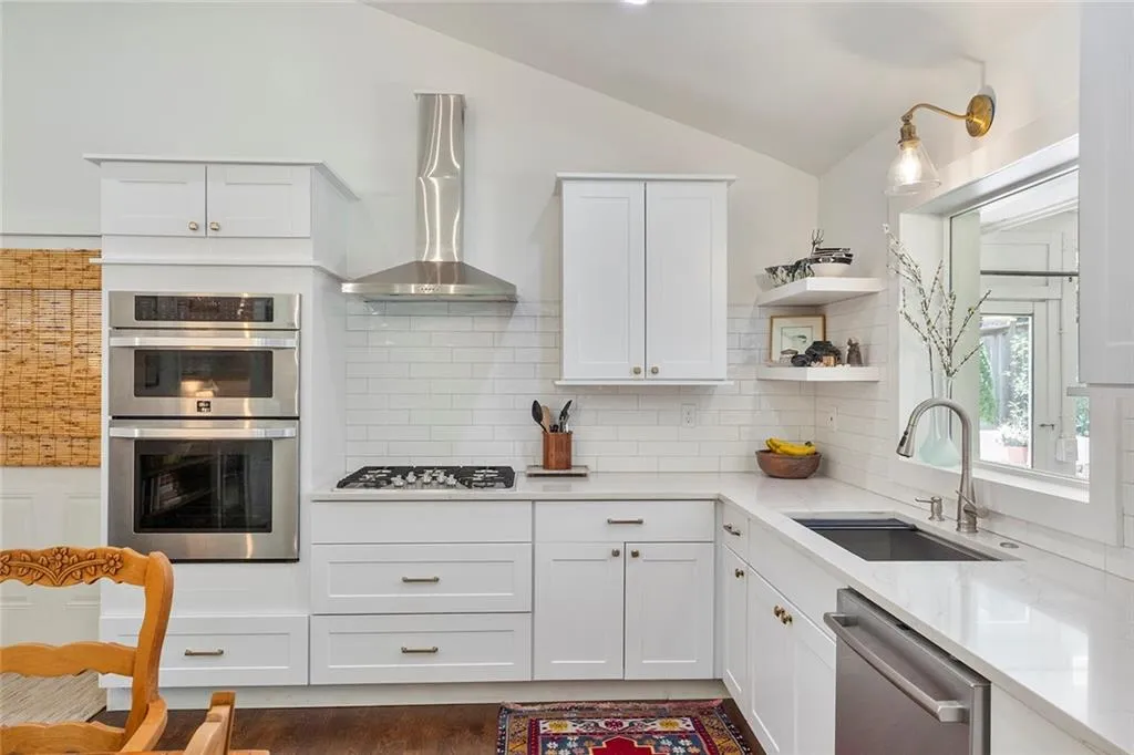 Kitchen with lofted ceiling, open shelves, appliances with stainless steel finishes, wall chimney exhaust hood, and white cabinets