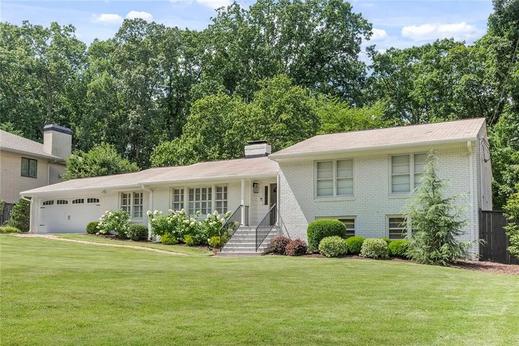 Split level home featuring brick siding, an attached garage, a front yard, and a chimney