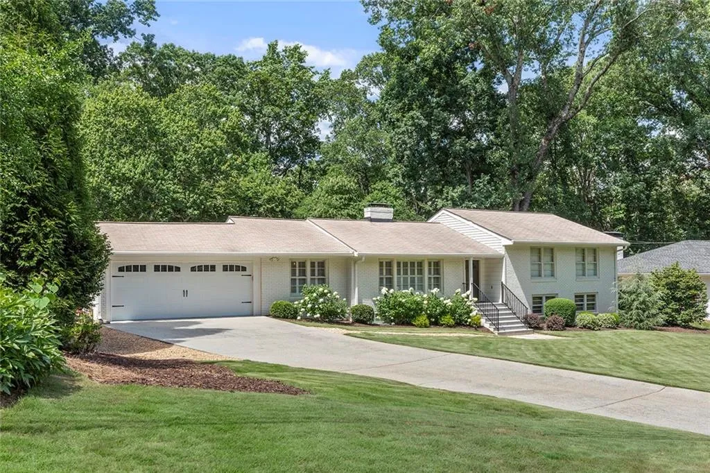 Split level home with concrete driveway, an attached garage, a chimney, a front lawn, and brick siding