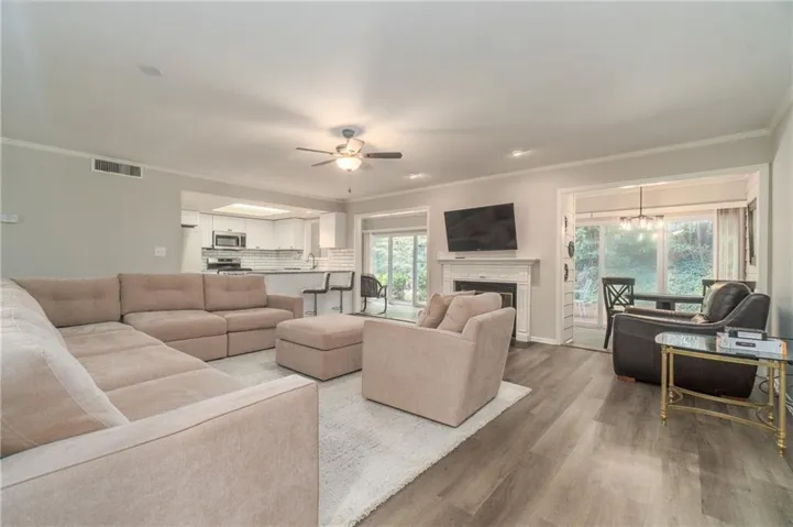Spacious living area featuring wood-finish flooring, a white mantel fireplace, ceiling fan.