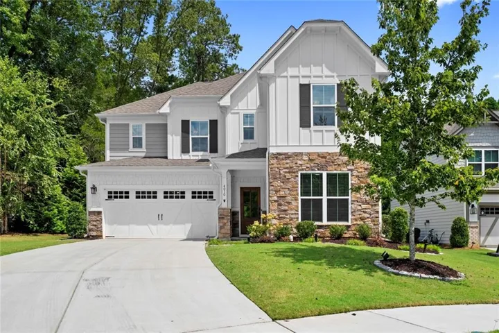 Two-story residence featuring a stone and siding exterior, an attached two-car garage, multiple windows with dark shutters, and a concrete driveway