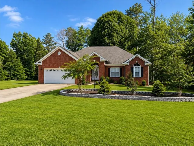 Brick exterior, attached two-car garage, concrete driveway, mature trees, and landscaped retaining wall