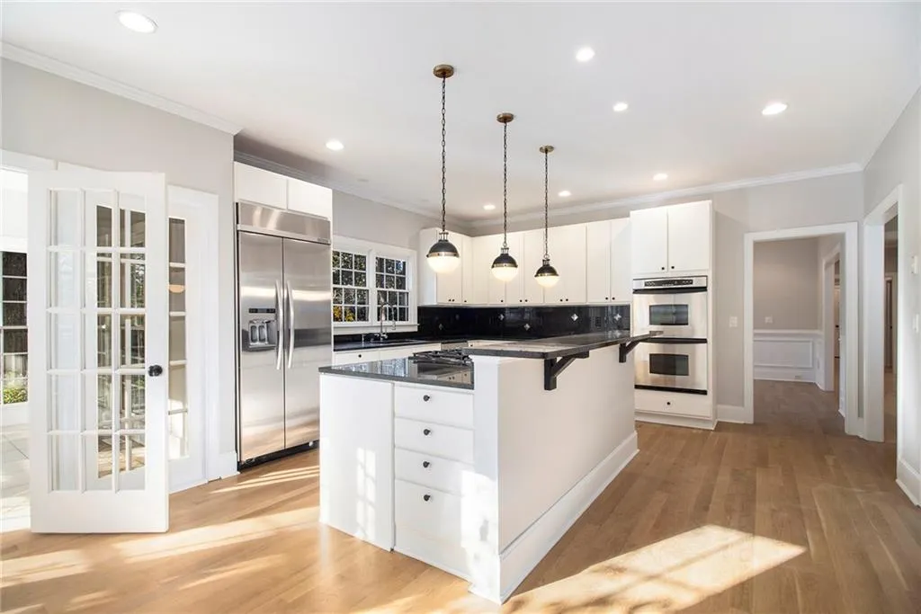 Kitchen with appliances with stainless steel finishes, a kitchen breakfast bar, white cabinets, crown molding, and pendant lighting