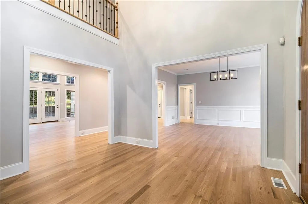 Corridor featuring a towering ceiling, light wood-style flooring, a chandelier, a decorative wall, and a wainscoted wall