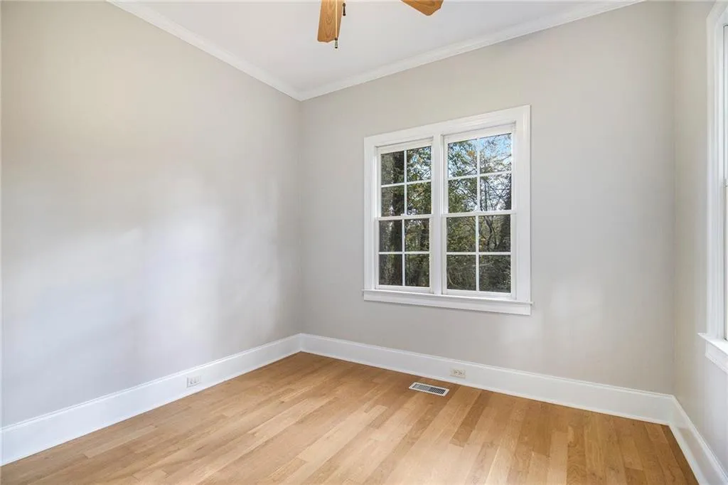 Empty room with ornamental molding, light wood-style floors, and a ceiling fan