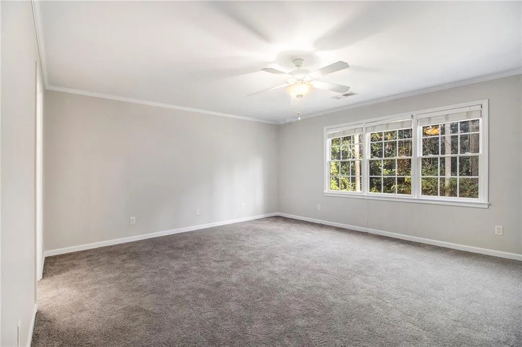 Empty room with carpet floors, crown molding, and a ceiling fan