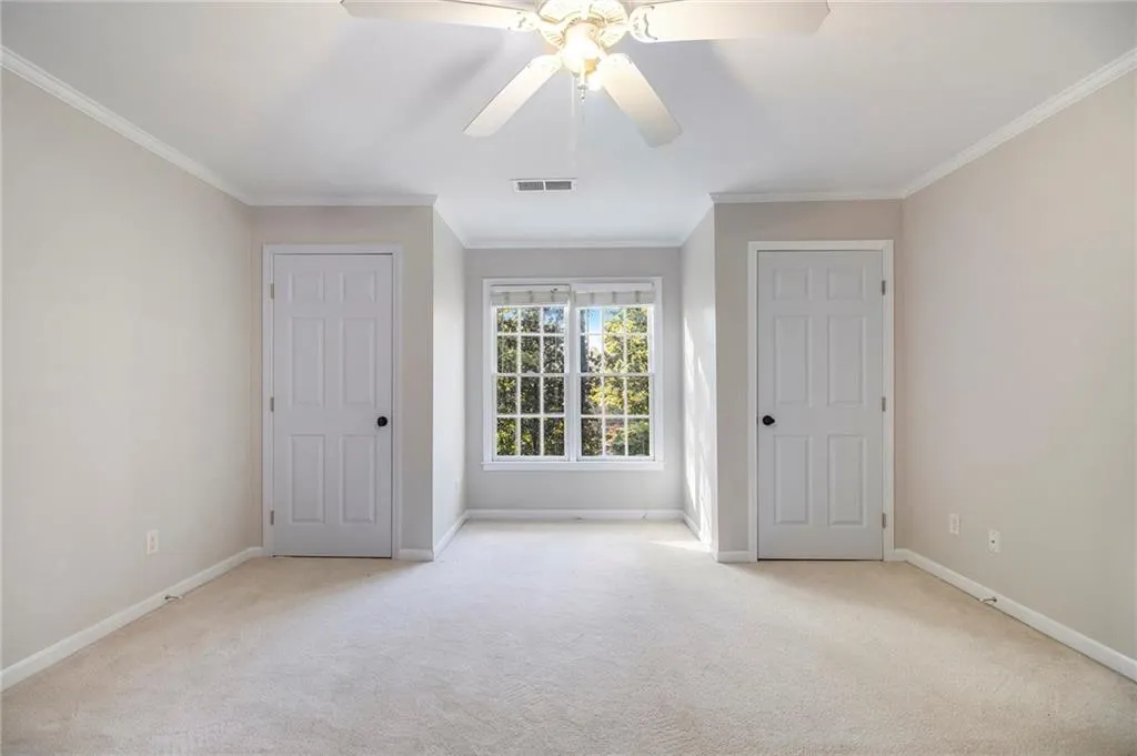 Unfurnished bedroom with light colored carpet, ornamental molding, multiple closets, and a ceiling fan