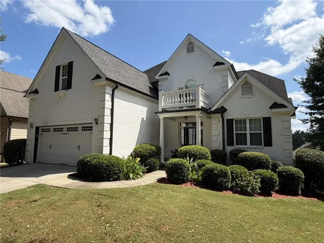 White brick exterior with a two-car garage, covered entry, and second-story balcony