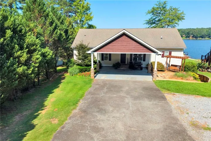 Waterfront property featuring a covered carport, shaker shingle gable accent, and a gravel and paved driveway