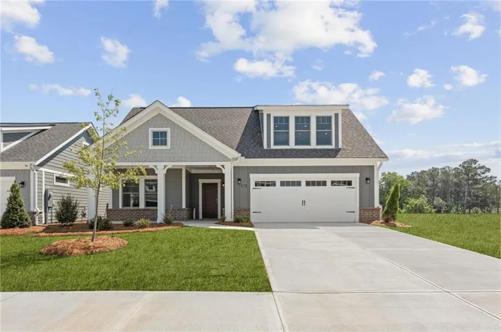 Modern Craftsman-style exterior featuring gray siding, a stone accent foundation, a covered entry porch, a white two-car garage, and a dormer with multiple windows
