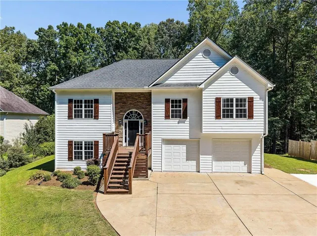 White siding exterior with a dark shingle roof, stone accent columns, and a front entry deck with wooden stairs