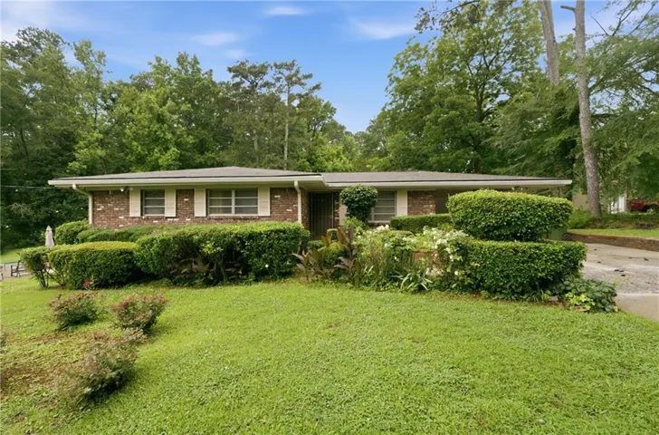 Brick exterior featuring white window shutters, mature landscaping, a paved driveway, and a sloped lawn
