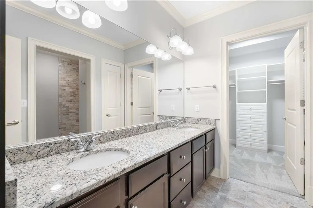 Full bathroom featuring a spacious closet, double vanity, and crown molding