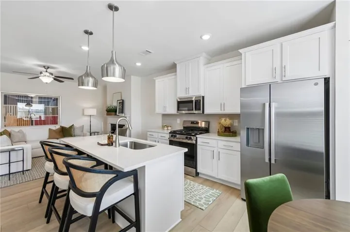 Open-concept kitchen with white shaker cabinetry, stainless steel appliances, a center island with sink, and wood-finish flooring
