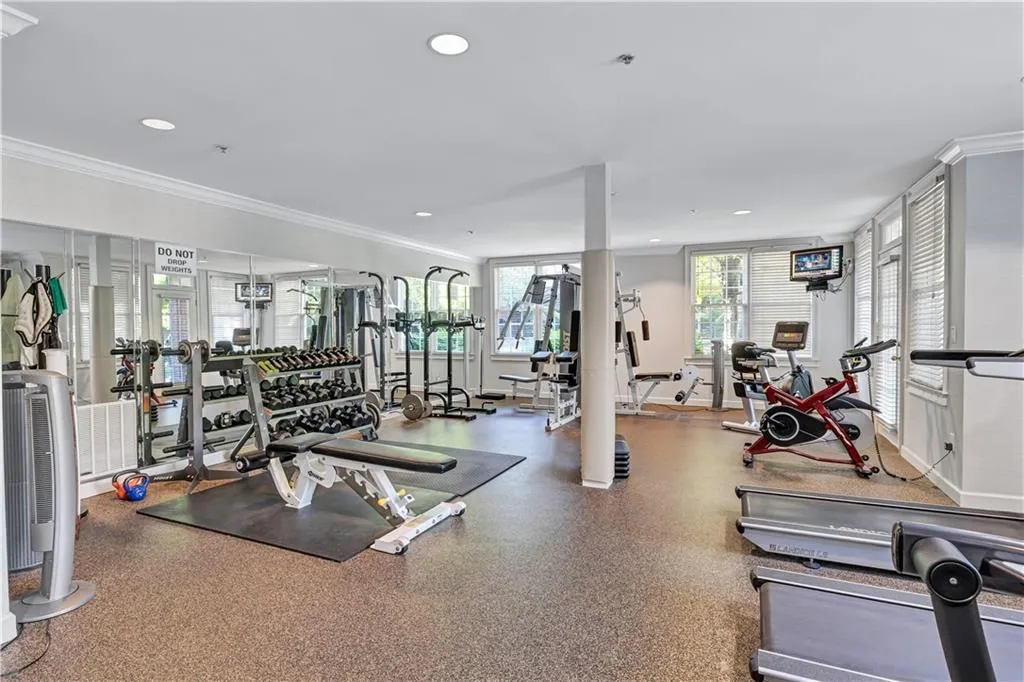 State-of-the-art fitness facility featuring cork composite flooring, extensive strength training equipment with dumbbell racks, cardio machines including stationary bikes and treadmills, mirrored walls with recessed lighting, and glass-enclosed storage areas for equipment organization