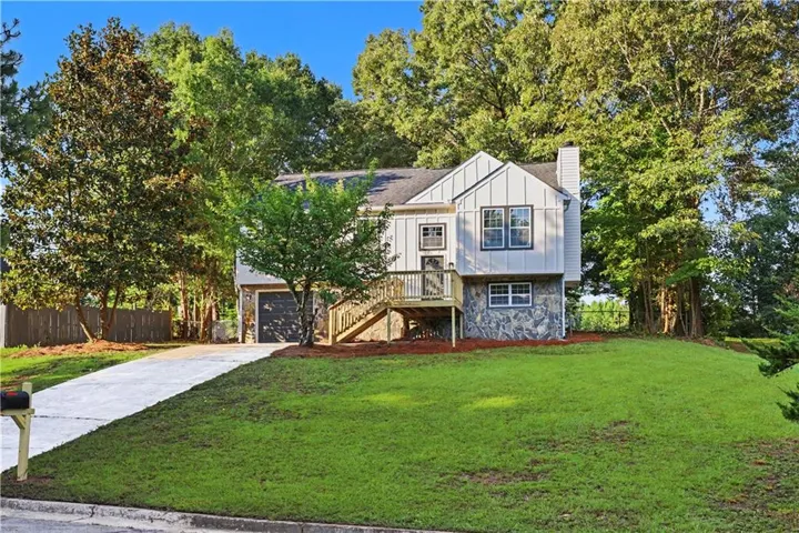 Split-level residence featuring a stone and siding exterior, a prominent front deck with wooden railings, and a two-car garage with a dark-colored door