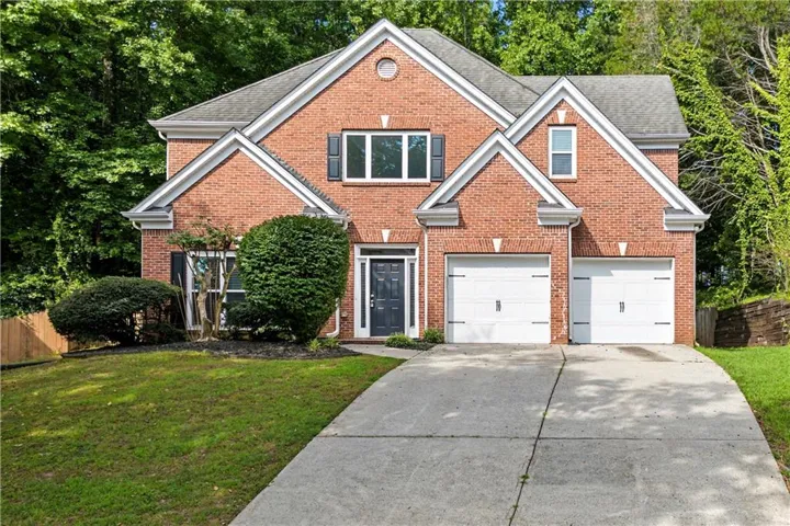 Red brick exterior with white trim, a two-car garage, a dark entry door, and mature landscaping