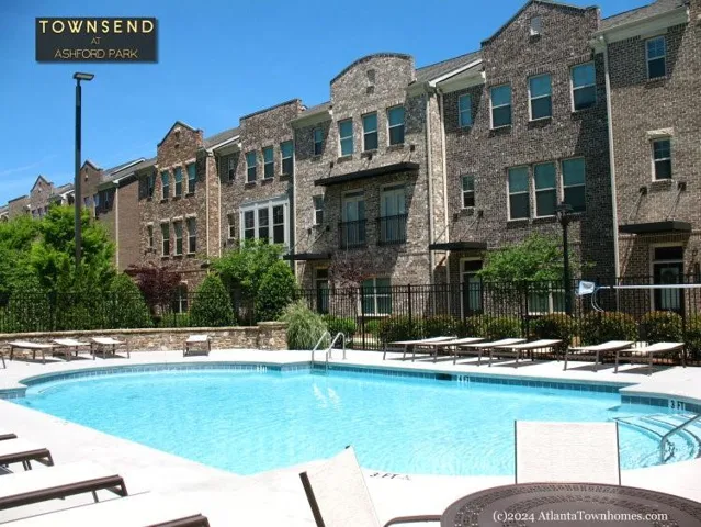 Community swimming pool with an expansive deck, complemented by brick-clad multi-story residences featuring multiple windows and balconies