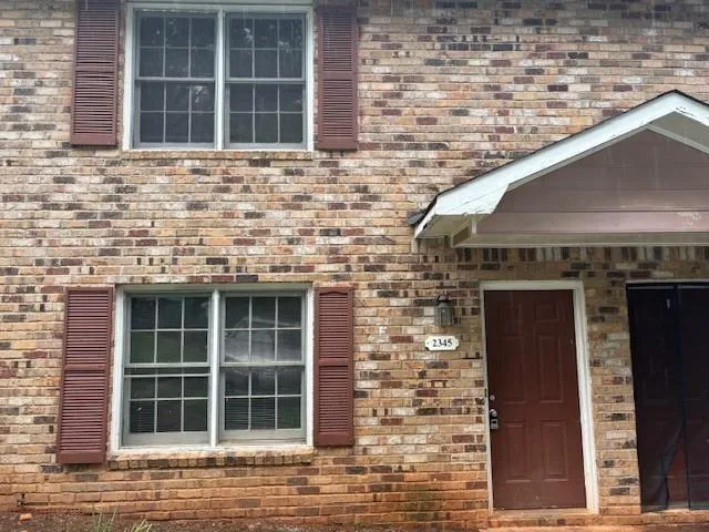 Brick exterior featuring red-brown shutters, a brown panel door, and an entryway awning