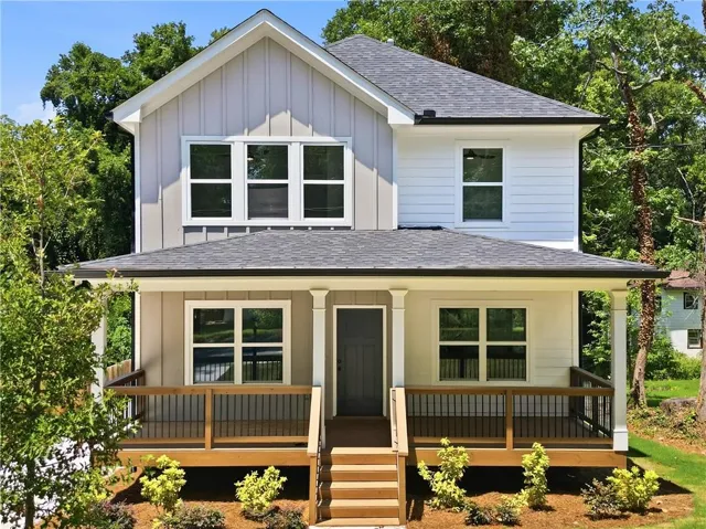 Modern two-story residence featuring a covered front porch with wood flooring and dark railings, multi-pane windows, and a dark asphalt shingle roof