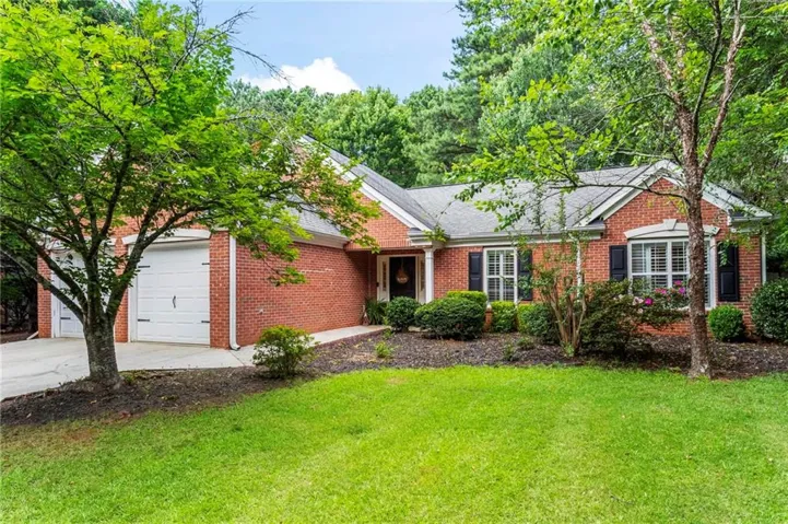 Brick exterior residence featuring a two-car garage, mature landscaping, bay window, and a shaded front entrance