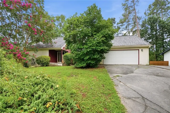 Ranch-style residence featuring a two-car garage, established front yard landscaping, and a red front entry