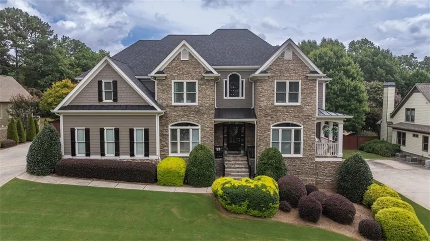 Stately multi-story residence featuring a stone and siding facade, dark shingle roof, and a covered front entry