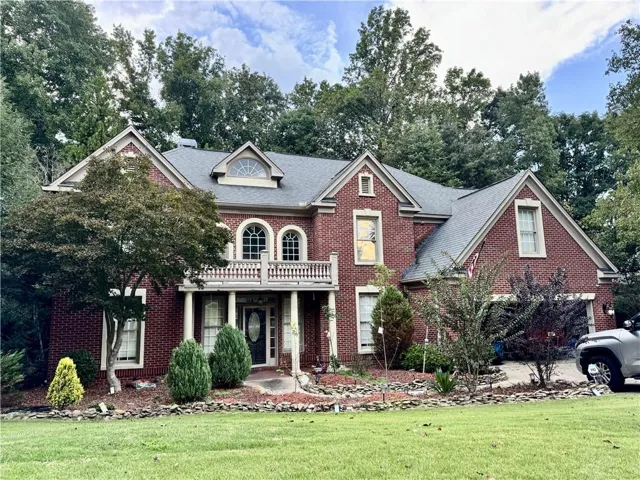 Brick exterior with a gray shingle roof, featuring a second-story balcony with white balusters