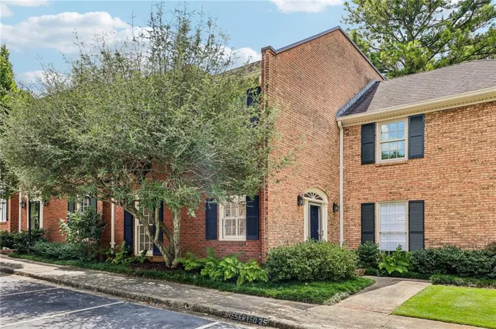 Brick exterior featuring multiple windows with black shutters, a gabled roof, and established landscaping