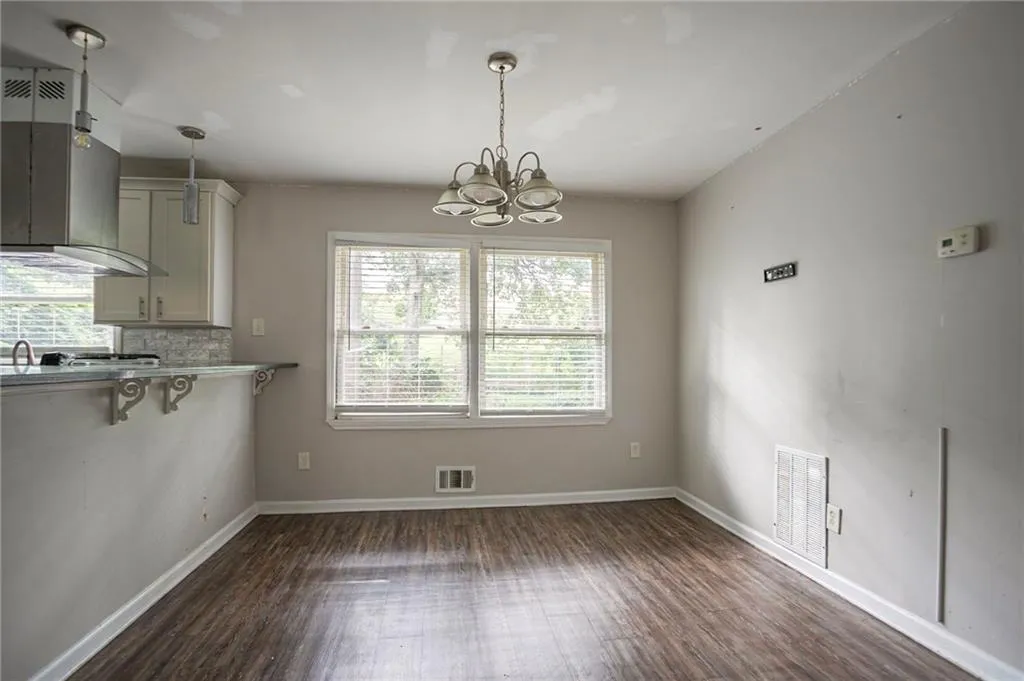 Unfurnished dining area featuring dark wood-style flooring and a chandelier