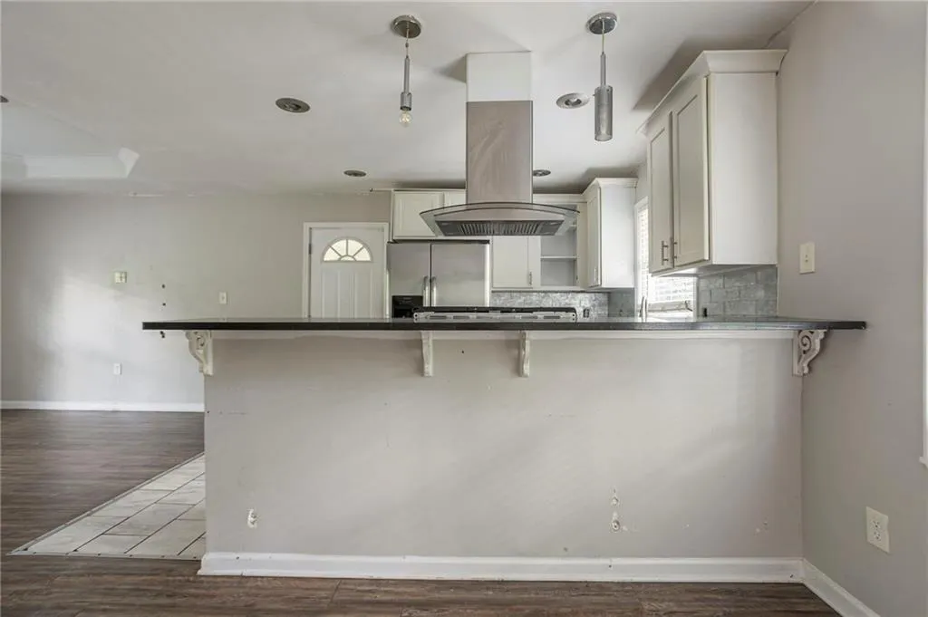 Kitchen featuring stainless steel fridge, island range hood, dark wood finished floors, and a breakfast bar