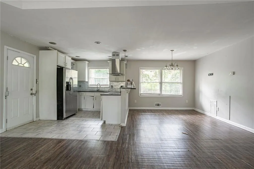 Kitchen with stainless steel refrigerator with ice dispenser, wall chimney exhaust hood, light wood-type flooring, open floor plan, and dark countertops